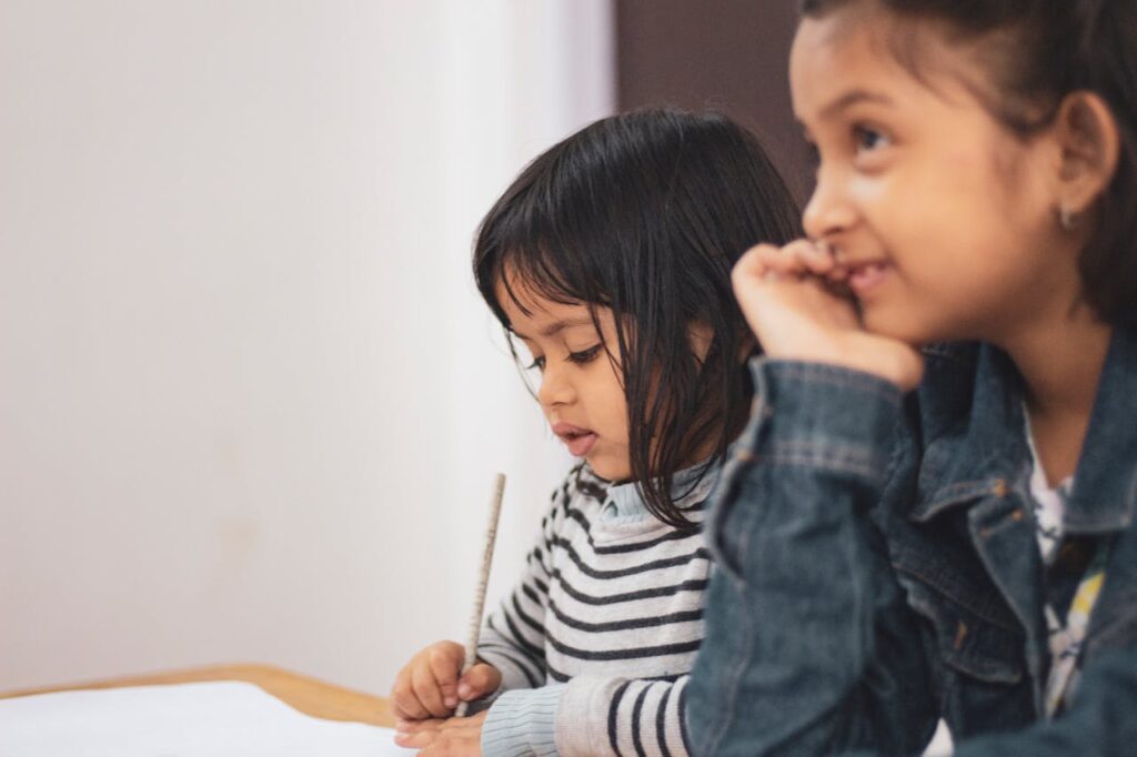 Two young girls joyfully engaged in creative learning indoors, capturing a candid moment of togetherness.